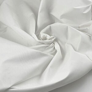May include: White fabric with a smooth texture, folded and arranged in a spiral shape. The fabric is soft and appears to be lightweight.