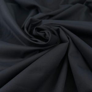 Könnte beinhalten: Nahaufnahme eines dunkelmarineblauen Stoffes mit weicher, fließender Textur. Der Stoff ist drapiert und gewirbelt, wodurch Schatten und Lichtreflexe entstehen, die seine glatte Oberfläche hervorheben. Das Material scheint ein mittelschweres Textil zu sein, das für verschiedene Nähprojekte geeignet ist.
