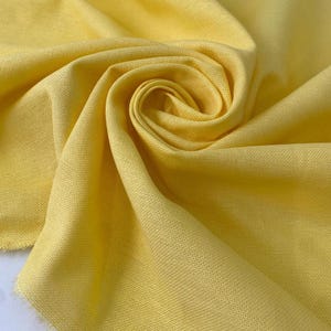 Puede incluir: Primer plano de una tela amarilla brillante con una textura tejida. La tela está recogida y arremolinada, creando pliegues y sombras. El color es un amarillo vibrante y soleado.