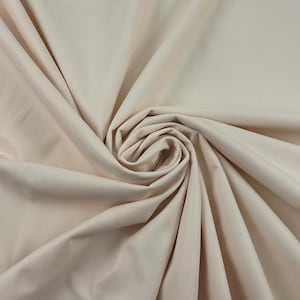 May include: A close-up of a swirl of light beige fabric. The fabric is smooth and appears to be a medium weight material. The folds and curves create a sense of depth and texture, with highlights and shadows adding visual interest.