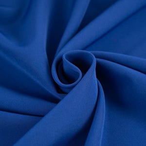 Pode incluir: Um close-up de um tecido azul royal liso. O tecido está dobrado e drapeado, mostrando sua textura macia.