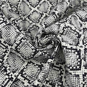 Peut inclure: Un tissu présentant un motif peau de serpent noir et blanc à fort contraste. Le matériau est drapé pour montrer des plis et une texture, affichant un motif géométrique d'écailles répétitif sur toute la surface avec des lignes noires.