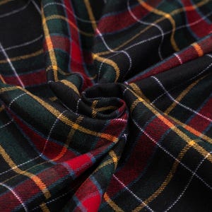 May include: Close-up of a folded fabric with a traditional tartan pattern. The design features a black base with intersecting lines in red, green, yellow, and white. The fabric is soft and has a slight sheen.