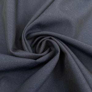 Könnte beinhalten: Ein einfarbiger schwarzer Stoff mit einer sichtbaren Webstruktur, der tiefe Falten und weiche Drapierungen aufweist, die natürliche Schatten auf der Oberfläche erzeugen. Das Material hat ein mattes Finish und eine gleichmäßige dunkle Farbe.