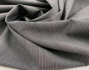 May include: Gray and white striped fabric with a subtle sheen. The fabric is folded and draped, showing the texture and drape of the material.