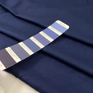 Może przedstawiać: Próbka granatowej tkaniny o teksturowanym splocie. Karta kolorów Pantone przecina tkaninę, prezentując odcienie niebieskiego, od jasnego do ciemnego. Karta zawiera nazwy i kody kolorów.