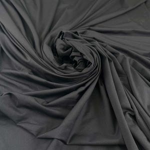 May include: A close-up of a large piece of black fabric, arranged in a spiral. The fabric appears soft and flowing, with subtle variations in texture and shadow, creating depth and movement. The material is likely suitable for clothing or home decor.