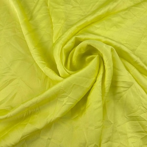 May include: A vibrant neon yellow fabric with a smooth, lustrous finish. The material is gathered into a central swirl, creating soft, flowing folds and deep shadows that highlight the reflective quality and bright, saturated color of the textile.