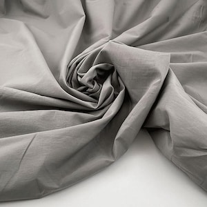 May include: A close-up of grey fabric, arranged in soft folds and swirls. The material has a matte finish, with visible creases and shadows adding texture. The image conveys a sense of softness and subtle elegance, suitable for textiles.