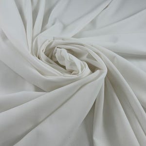 May include: A close-up shot of a white fabric, artfully arranged in soft folds and swirls. The fabric appears to be lightweight and smooth, with a subtle sheen. The folds create shadows and highlights, adding depth and texture to the image.