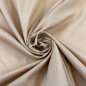 Puede incluir: Primer plano de una tela beige con un aspecto suave y texturizado. La tela está recogida y doblada, creando un patrón arremolinado. El color es un tono cálido y neutro, adecuado para varios proyectos de costura.