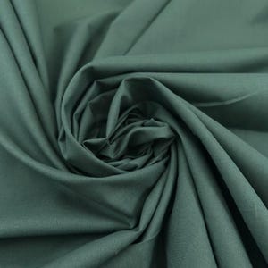 May include: Close-up of a dark teal fabric, tightly swirled to create a spiral pattern. The fabric has a smooth texture and appears to be a solid colour. The folds and shadows create depth and dimension, highlighting the fabric's drape.
