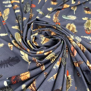 Puede incluir: Primer plano de una tela con fondo azul oscuro, cubierta con un estampado de plumas coloridas. Las plumas varían en tamaño y color, incluyendo tonos de marrón, naranja, verde y negro. La tela está doblada, creando sombras y profundidad.