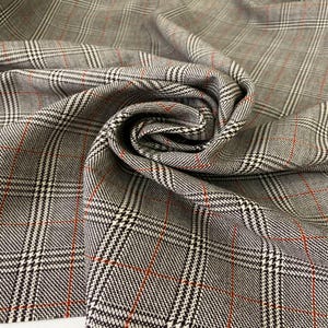May include: A close-up shot of grey fabric with a traditional plaid design. The material has a woven texture with intersecting black, white, and red lines. The fabric is folded, revealing the repeating pattern and the texture of the material.