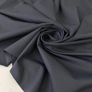 Può includere: Tessuto blu navy scuro con morbide pieghe e un motivo a vortice. Il tessuto appare liscio e opaco, con una leggera lucentezza. L'immagine mostra la consistenza e il drappeggio del materiale, adatto per abbigliamento o arredamento.