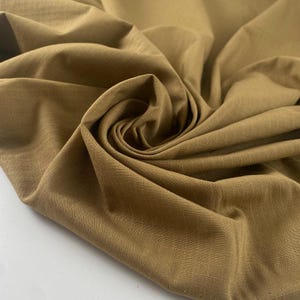 May include: Close-up of a tan-colored fabric with a subtle grid pattern. The fabric is tightly woven and appears to be a durable material, with visible folds and textures. The overall tone is a warm, earthy color.