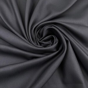 Peut inclure: Un tissu gris anthracite uni avec une texture lisse et mate. Le matériau est disposé en spirale centrale, créant des plis profonds et fluides ainsi que des ombres qui rayonnent depuis le point central sur toute la surface du tissu.