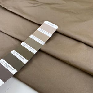Könnte beinhalten: Gefalteter, beigefarbener Stoff mit einer Pantone-Farbkarte. Die Karte zeigt verschiedene Brauntöne, darunter "Chocolate Chip" und "Cub". Der Stoff wirkt glatt und weist feine Falten auf.