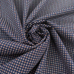 Könnte beinhalten: Ein marineblauer Stoff mit einem sich wiederholenden geometrischen Muster aus kleinen weißen Quadraten mit zentrierten braunen Punkten. Das Material ist in der Mitte gerafft und erzeugt weiche Falten und Schatten, die das gleichmäßige Gitterdesign betonen.
