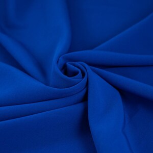 Pode incluir: Um close-up de um tecido azul royal liso com uma textura suave e fluida. O tecido é dobrado e drapeado, criando uma sensação de movimento e elegância.