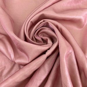 Peut inclure: Un morceau de tissu rose poudré doté d'une finition lisse et lustrée. Le matériau est rassemblé en une spirale centrale, créant des plis profonds et fluides ainsi que des ombres qui soulignent la texture satinée et réfléchissante du textile.