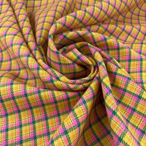 Puede incluir: Primer plano de una tela vibrante con un patrón de cuadros. La tela presenta un patrón de diamantes repetido en amarillo, rosa y verde. La tela está arremolinada, mostrando las variaciones de textura y color.
