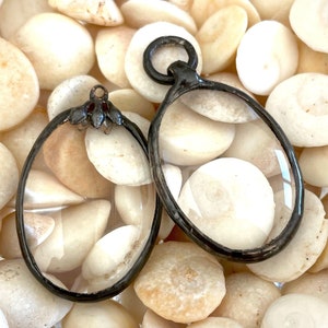 May include: Two antique silver-toned oval-shaped magnifying glasses with clear glass lenses, resting on a bed of white seashells.