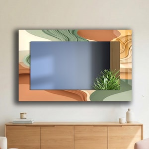 May include: A modern wall mirror with a rectangular blue center, framed by layered abstract shapes in shades of brown, green, and beige. A small green plant is placed on the right side of the mirror. The mirror is mounted above a wooden cabinet.