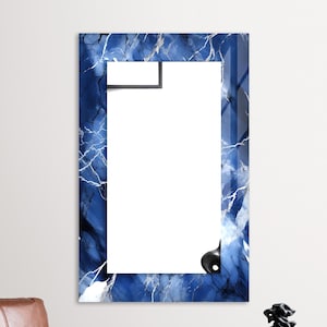 May include: A blue and white abstract patterned mirror with a white frame. The mirror is hanging on a white wall.