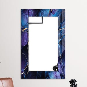 Pode incluir: Um espelho retangular com uma moldura de design de mármore abstrato azul e dourado. A moldura tem um fundo azul escuro com veios dourados e acentos roxos.