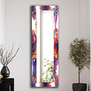 Pode incluir: Um espelho alto e retangular com uma borda de design de penas vibrantes e coloridas. As penas apresentam tons de roxo, laranja, vermelho e amarelo. O espelho é exibido em um quarto branco com uma mesa lateral preta e uma planta em vaso.