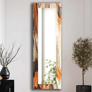 May include: A full-length rectangular mirror with a decorative frame. The frame features a layered design in shades of brown, orange, and cream, creating a textured, abstract pattern. The mirror is positioned against a white wall, with a plant visible in the reflection.