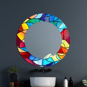 Peut inclure: Un miroir rond avec un motif de vitrail coloré dans des tons de rouge, orange, jaune, vert, bleu et violet. Le miroir est suspendu à un mur gris foncé au-dessus d'un lavabo en porcelaine blanche.