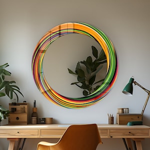 Puede incluir: Un espejo redondo con un marco colorido y rayado. El marco está hecho de múltiples capas de finas tiras coloridas que crean un patrón de remolino. El espejo está colgado en una pared blanca sobre un escritorio de madera con una silla amarilla.