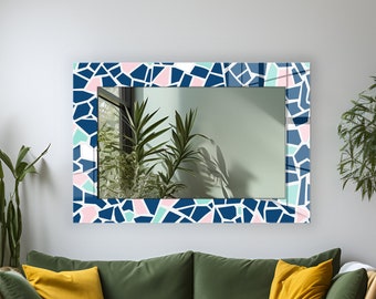 May include: A green velvet sofa with two yellow throw pillows and a white throw blanket. A mirror with a blue and pink geometric pattern hangs above the sofa.