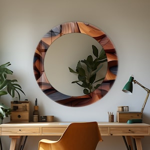 May include: A round mirror with a brown and blue abstract design frame. The mirror is hanging on a white wall above a wooden desk with a yellow chair.