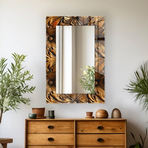 Pode incluir: Um espelho retangular com uma moldura dourada decorativa com um design floral intrincado. O espelho está pendurado em uma parede branca acima de uma cômoda de madeira com gavetas.