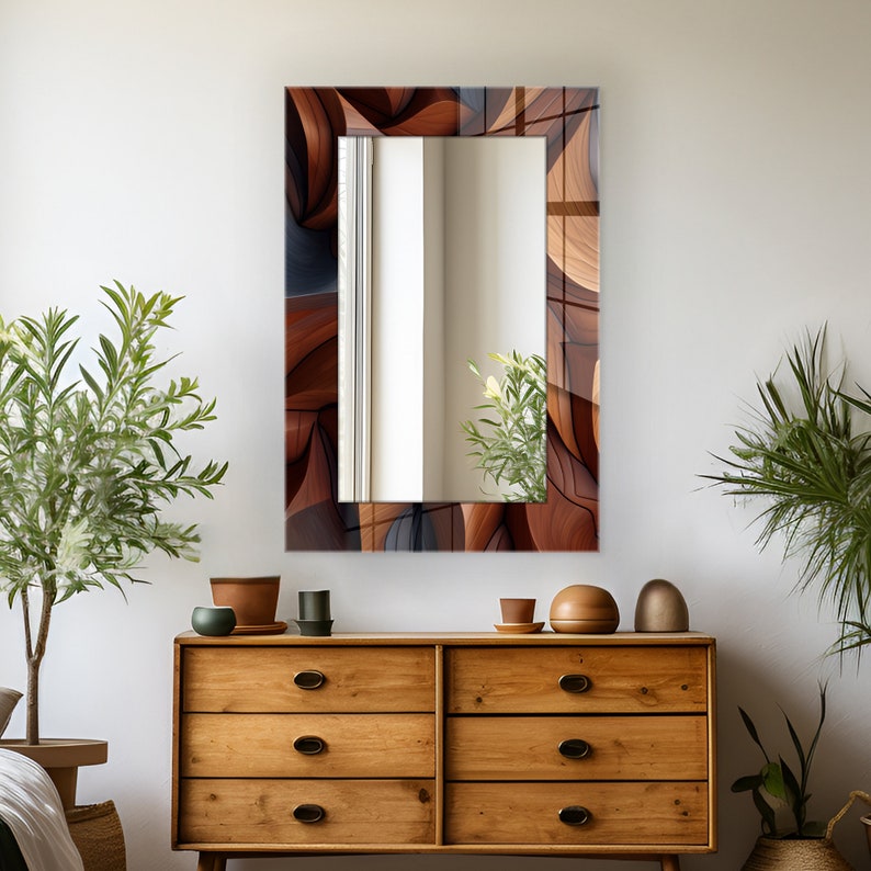Pode incluir: Um espelho retangular com uma moldura de design abstrato marrom, cinza e preto. O espelho est&aacute; pendurado em uma parede branca acima de uma c&ocirc;moda de madeira com gavetas.