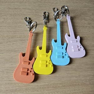 Könnte beinhalten: Vier Miniatur-Elektrogitarren-Schlüsselanhänger in verschiedenen Farben: Orange, Gelb, Blau und Pink. Jeder Schlüsselanhänger hat einen silbernen Metallring.