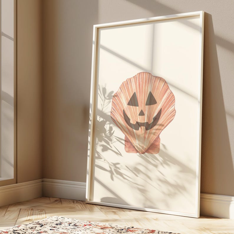 May include: A white framed print of a seashell with a jack-o'-lantern face. The seashell is a light orange colour with a dark orange outline. The jack-o'-lantern face is black with a white smile.