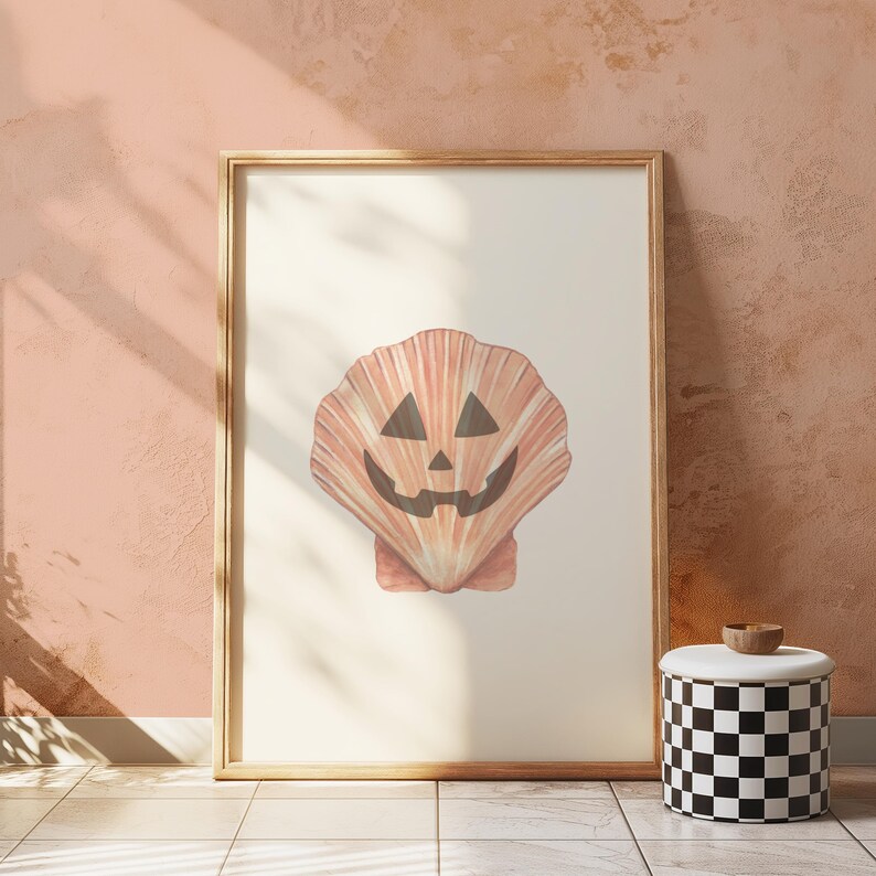 May include: A framed print of a seashell with a jack-o'-lantern face. The seashell is a light orange colour with a white background.