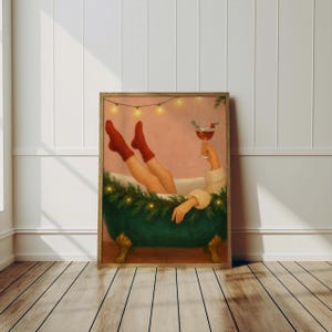 May include: A framed print depicts a person relaxing in a green clawfoot bathtub, wearing red socks and holding a cocktail. The tub is decorated with greenery and lights, creating a festive atmosphere. The artwork has a warm, inviting color palette.