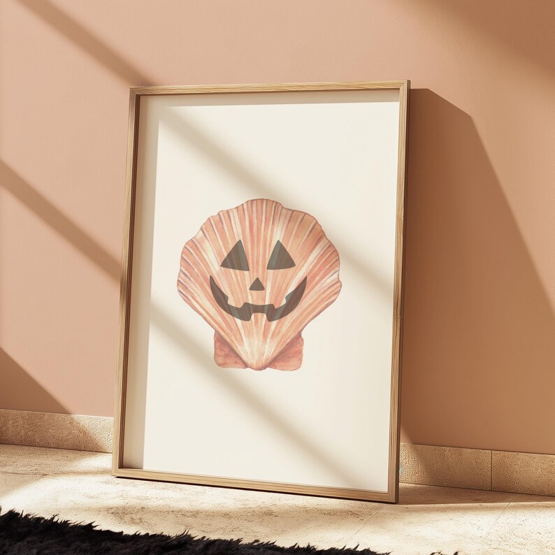 May include: A framed print of a seashell with a carved jack-o'-lantern face. The shell is a light orange colour with a white background.