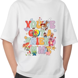 K&ouml;nnte beinhalten: Wei&szlig;es T-Shirt mit einem bunten Grafikdruck von Figuren aus dem Toy Story-Film-Franchise. Die Grafik zeigt den Text "You've Got a Friend in Me" mit den Figuren Woody, Buzz Lightyear, Jessie und anderen.