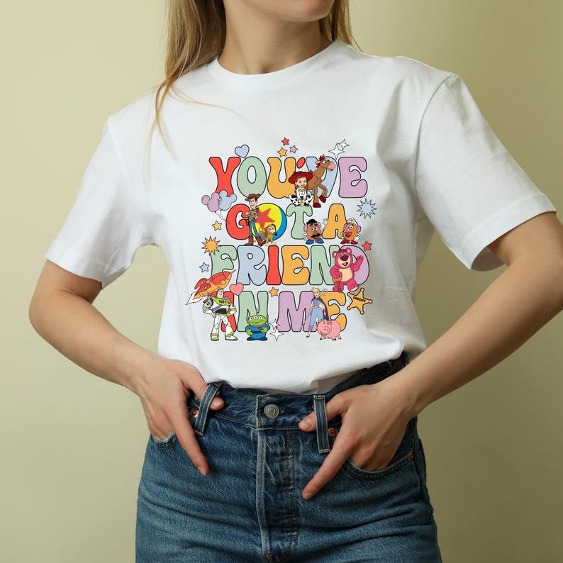 K&ouml;nnte beinhalten: Wei&szlig;es T-Shirt mit einem bunten Grafikdruck von Figuren aus dem Toy Story-Franchise. Der Text auf dem Shirt lautet "You've Got a Friend in Me."