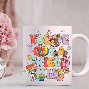 K&ouml;nnte beinhalten: Wei&szlig;e Keramik-Kaffeetasse mit einer bunten Grafik von Figuren aus dem Toy Story-Film-Franchise. Der Text auf der Tasse lautet "You've Got a Friend in Me".
