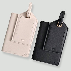 May include: Two luggage tags, one cream and one black, with gold-colored buckles and straps. The cream tag has the initials "CD" and the black tag has the initials "TW". Both tags have a textured appearance.