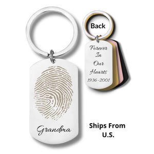 May include: A silver-toned metal keychain featuring a rectangular tag engraved with a tan fingerprint and the word Grandma. A second smaller tag labeled Back displays the text Forever In Our Hearts 1936-2001, with additional stacked tags in gold and black.