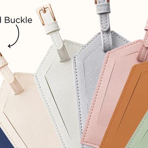 May include: A collection of colorful luggage tags with gold buckles. The tags are in various pastel colors, including cream, light gray, pink, and green. Each tag has a rectangular window for inserting a name card.