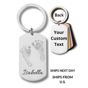 May include: A silver-colored keychain with a dog tag pendant featuring baby footprints and the name "Isabella." The keychain includes a ring and a smaller tag with the words "Your Custom Text" and "Back."